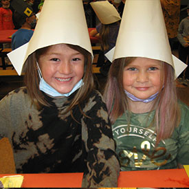 Two female students smiling and wearing paper hats